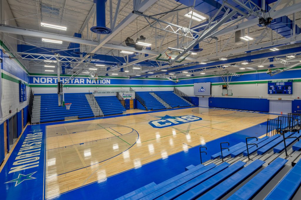 The renovated CNS High School gymnasium featuring new hardwood floors, updated blue bleachers, fresh paint, and modernized athletic equipment and press box.